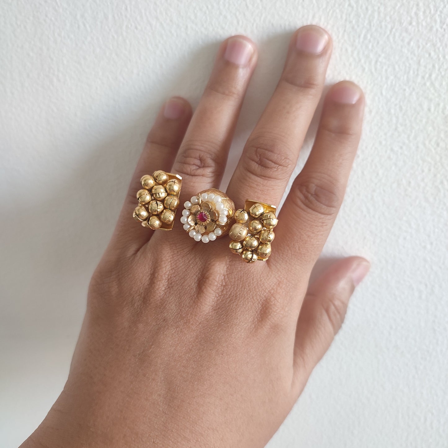 Hand wearing a gold ring with floral design on a white background