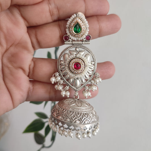 Decorative silver earrings with gemstones held in a hand against a neutral background