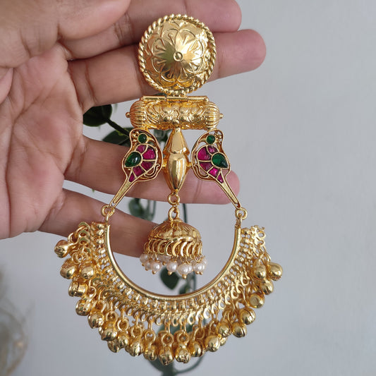 Gold earrings with intricate designs held in a hand against a neutral background
