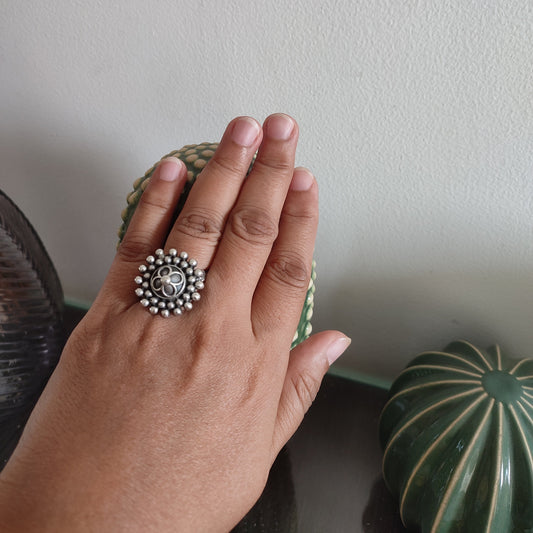 Hand wearing a silver ring with a decorative design on a neutral background