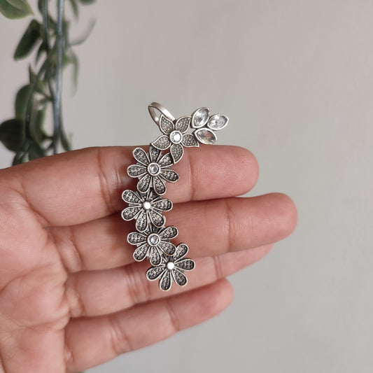 Silver floral earrings held in a hand with a neutral background