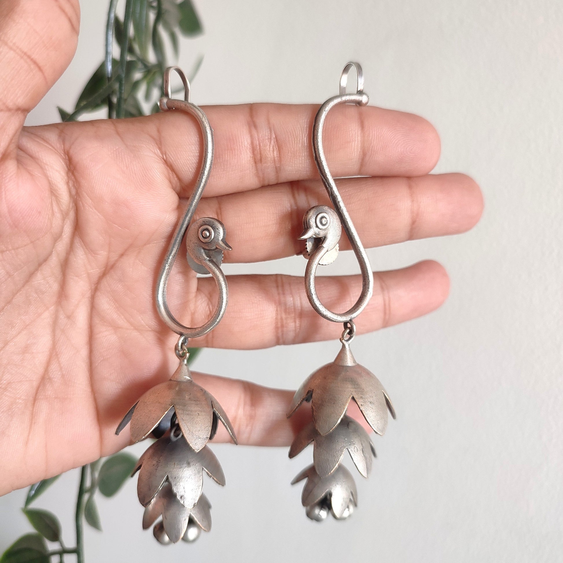 Silver floral earrings held in a hand with a light background