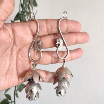 Silver floral earrings held in a hand with a light background