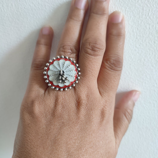 Hand wearing a decorative ring with a red and white design on a light background