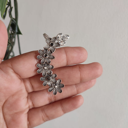 Silver floral earrings held in a hand against a neutral background