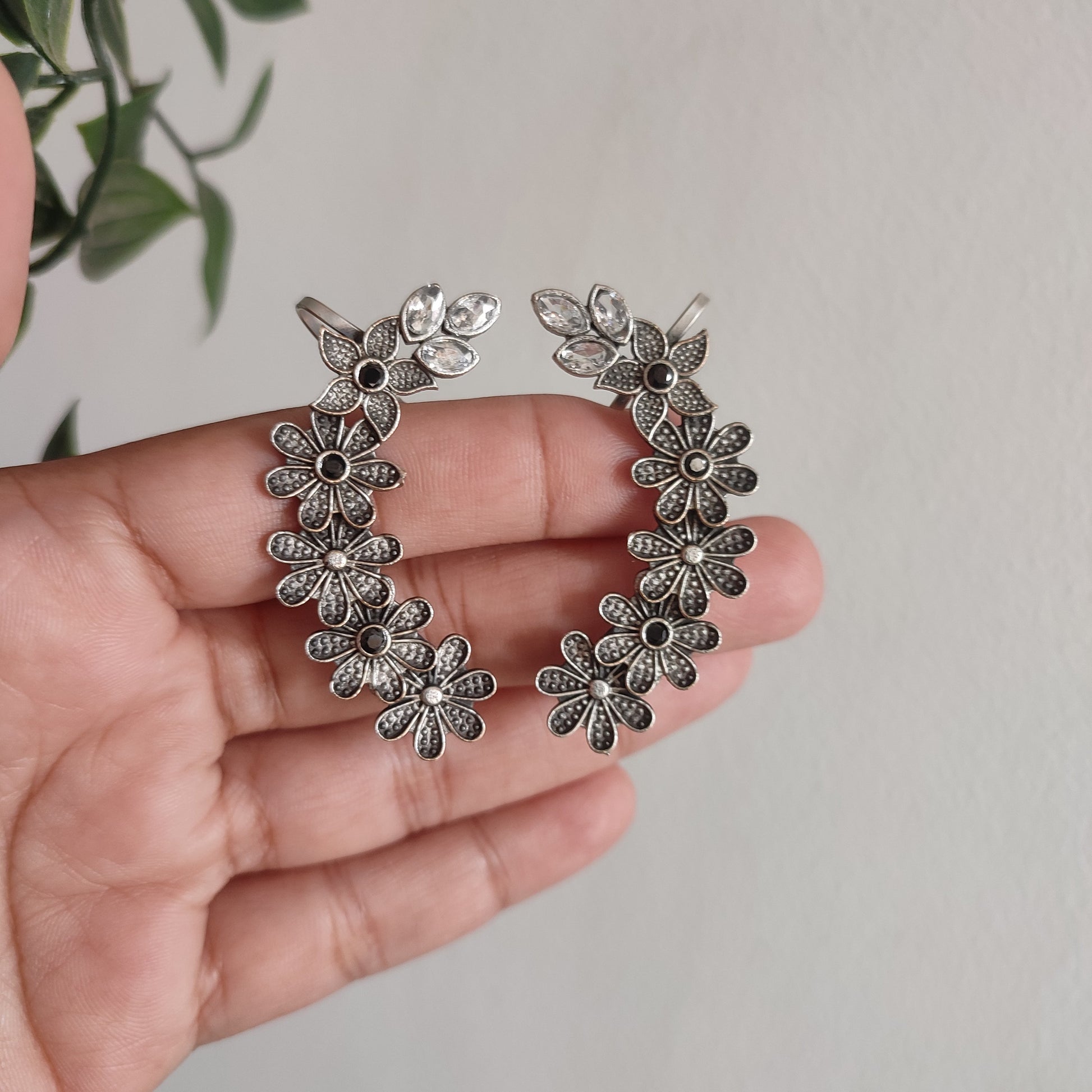 Silver floral earrings held in a hand with a light background