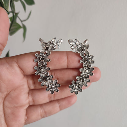 Silver floral earrings held in a hand against a neutral background