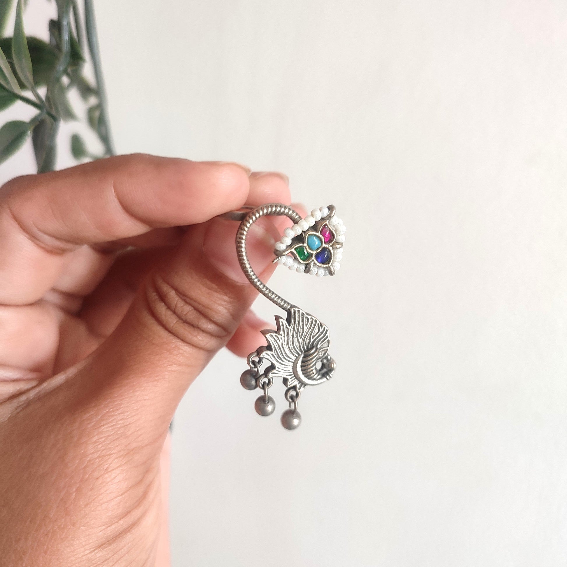 Hand holding a silver belly button ring with colorful gemstones against a white background