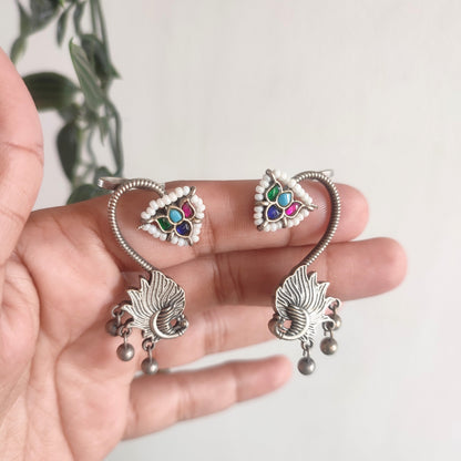 Silver earrings with colorful gemstones held in a hand against a light background